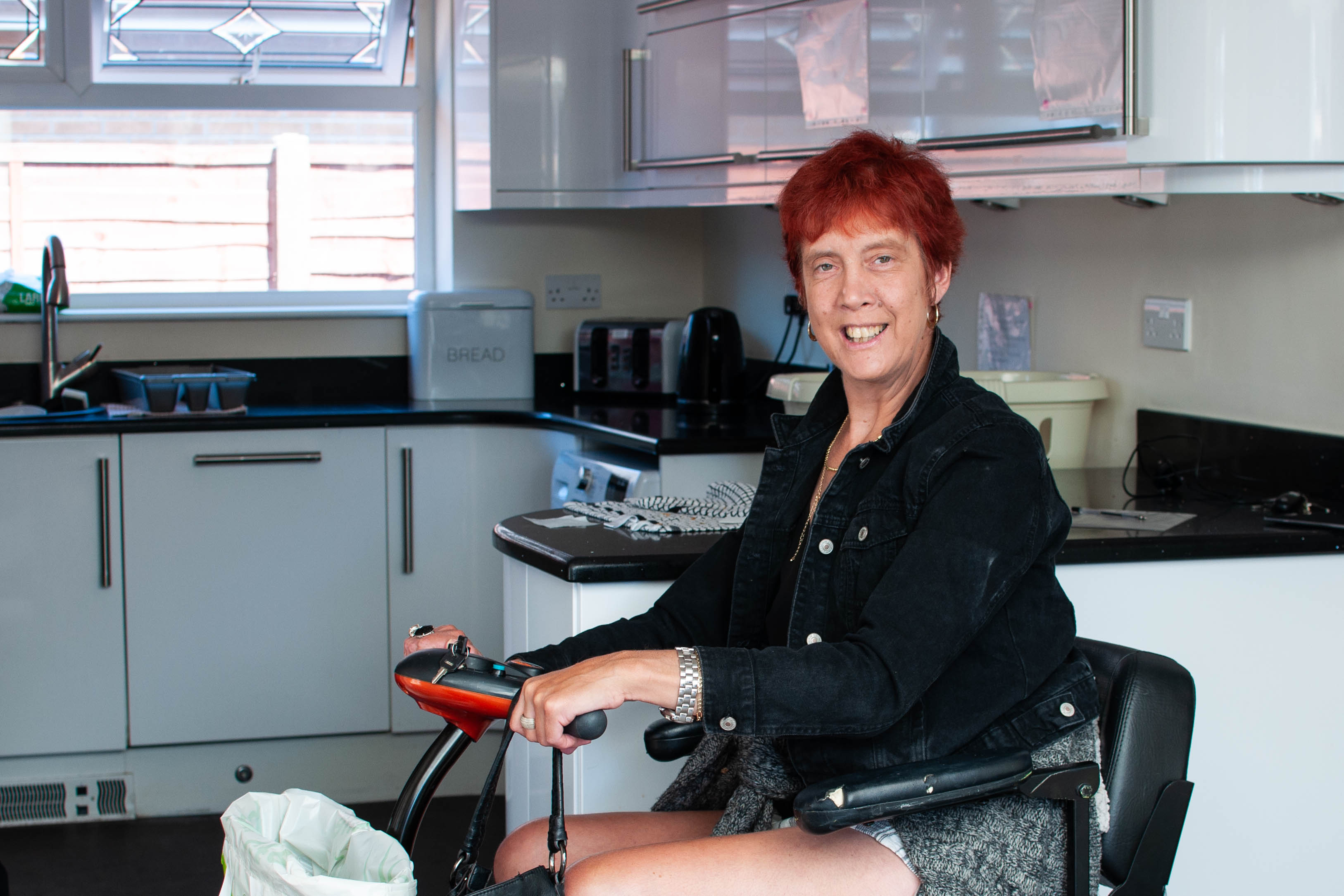 A woman with short red hair sitting on a mobility scooter smiling at the camera
