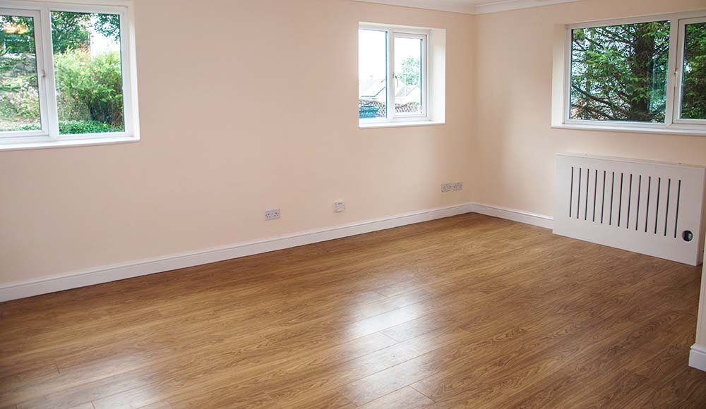 Empty living room with three windows and a wooden floor