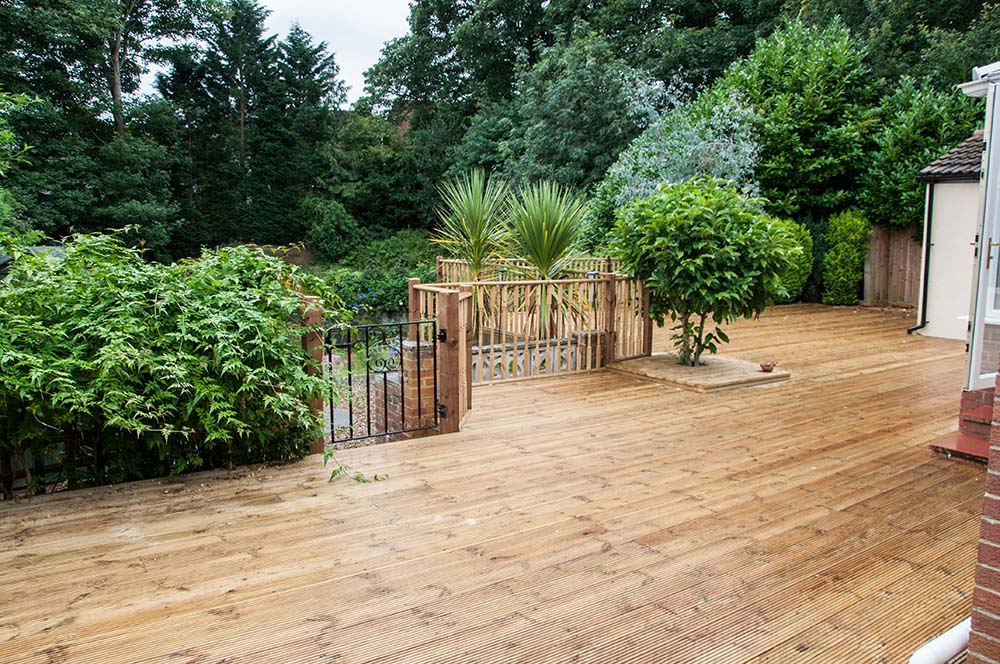 Large wooden deck area at back of house with stairs leading down into the garden