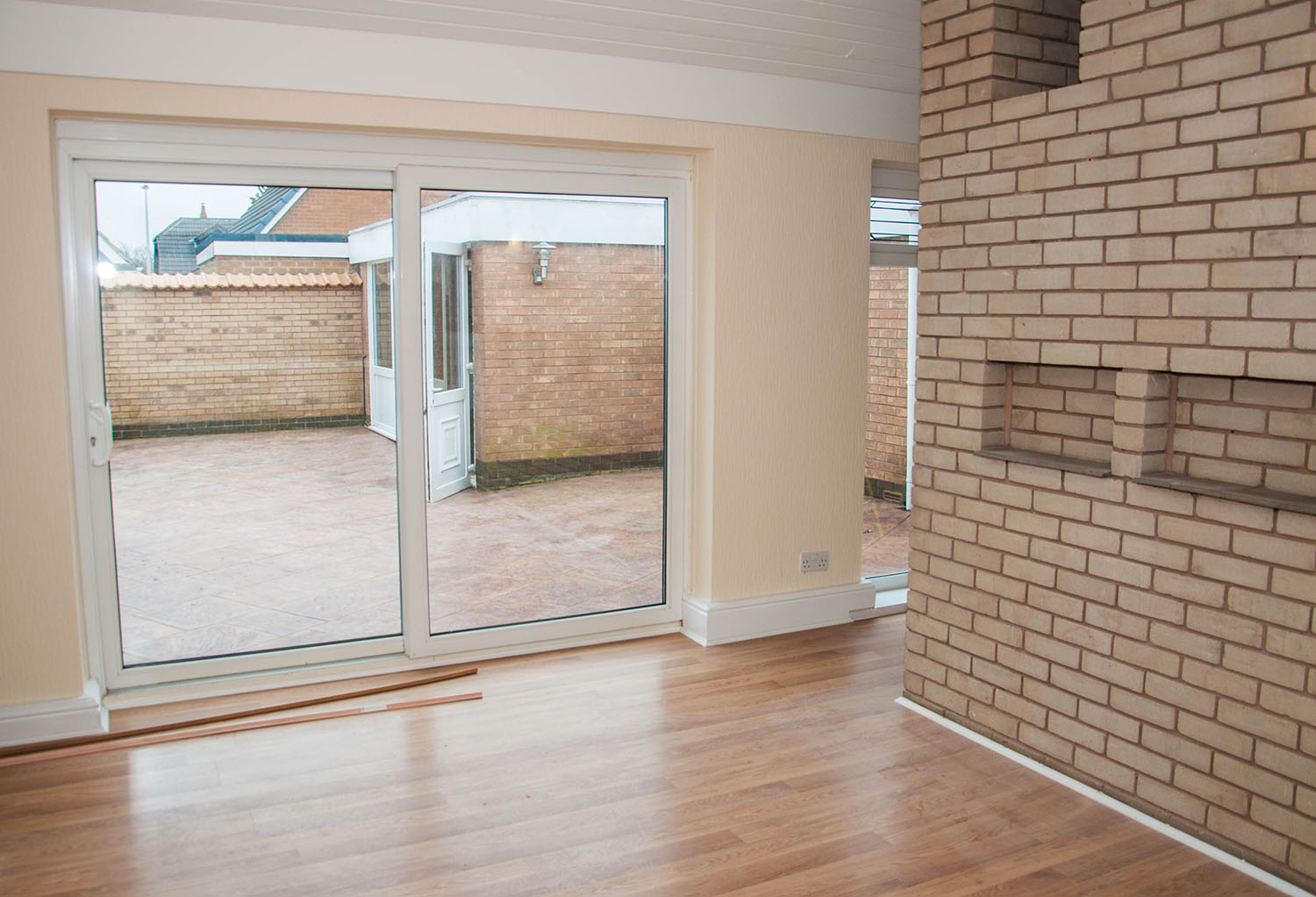 Living room with bricked wall and wooden floors and sliding doors opening out into the patio area