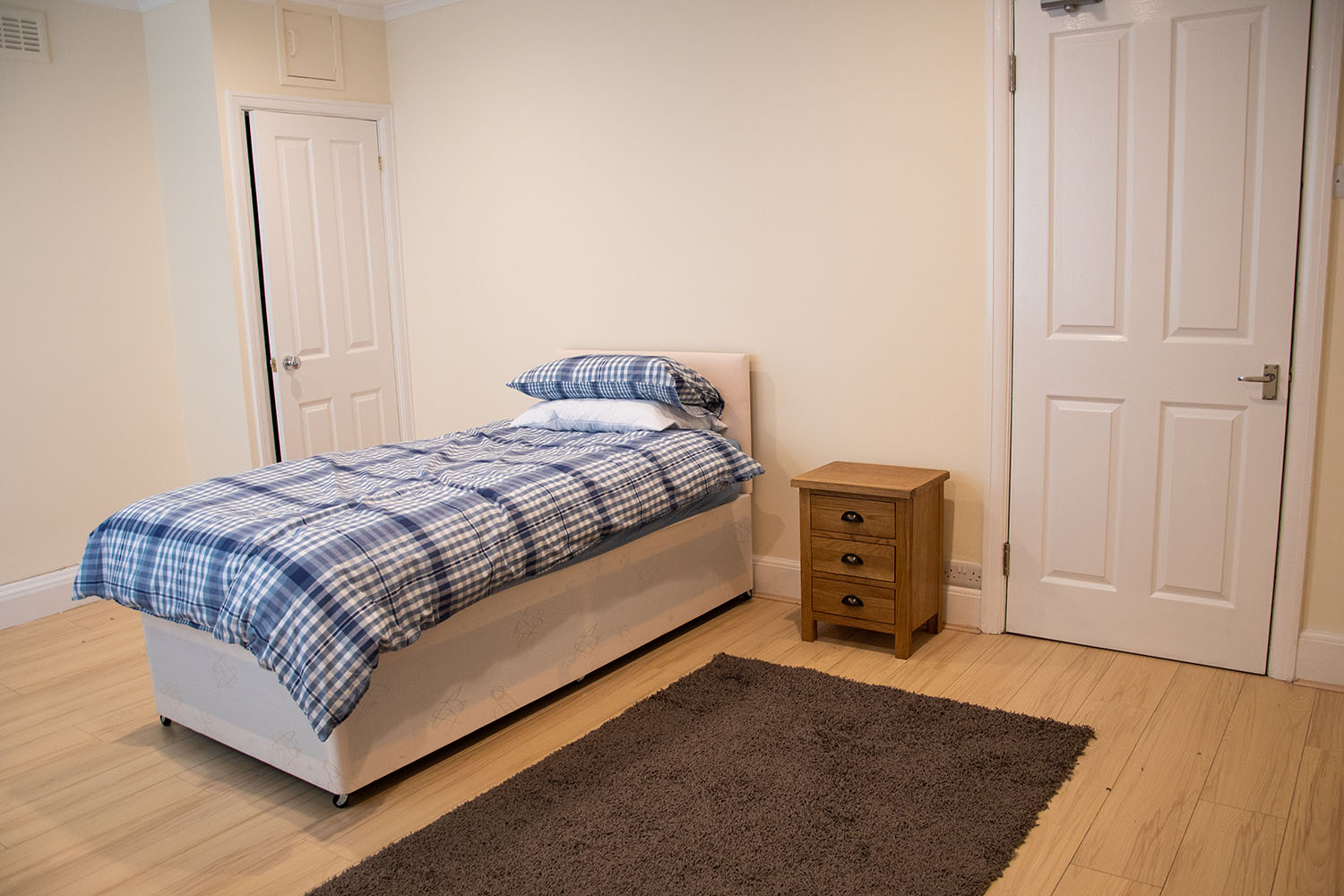 A bedroom with a single bed, bedside table and a brown rug in it