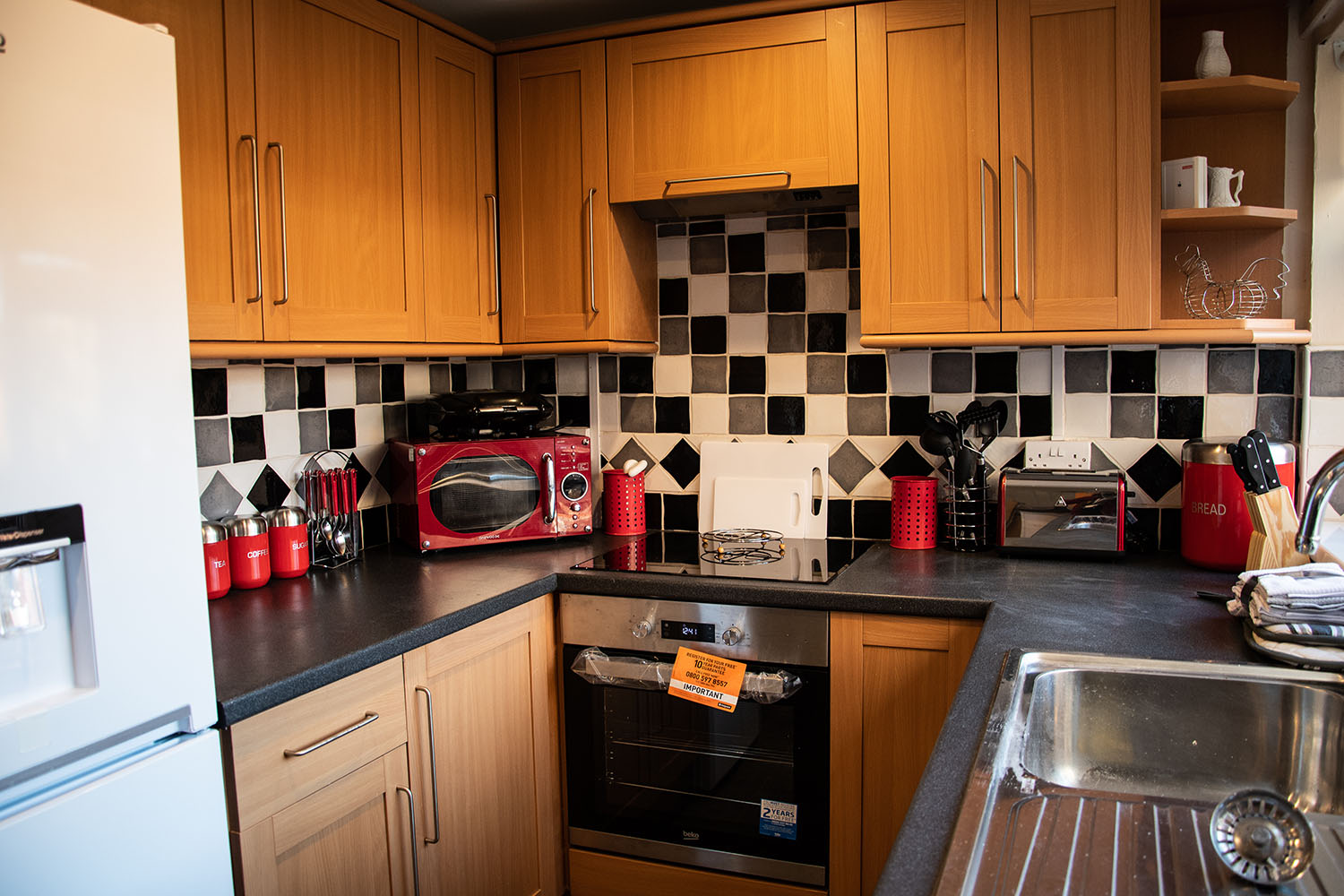 A kitchen with wooden cabinets and black, white and grey tiles and red appliances