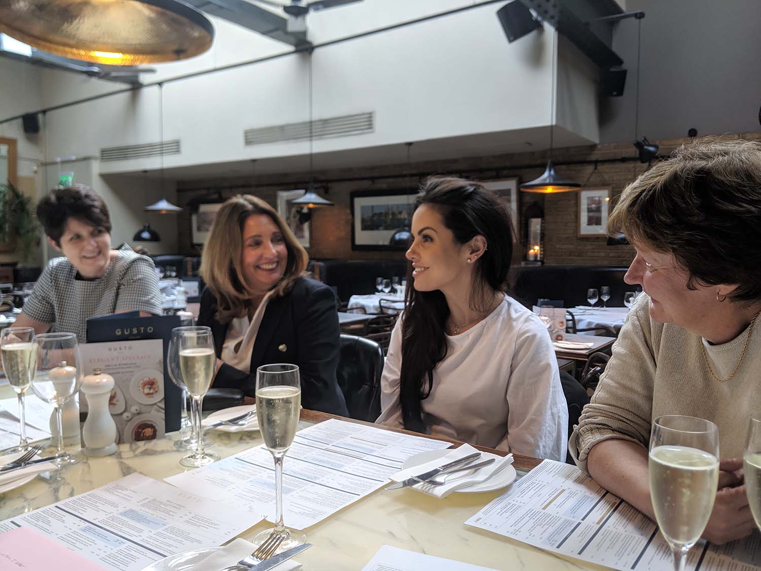 4 women sitting at a table in a resturant smiling at one another