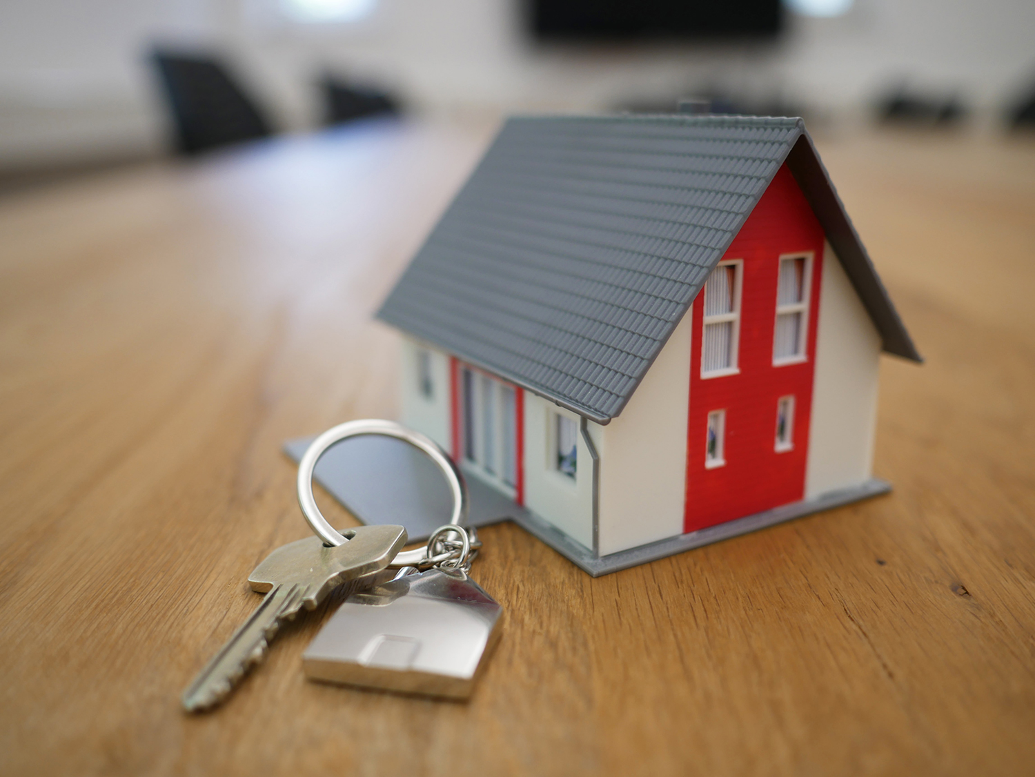 A key with a silver house keychain attached to it lying next to a small model of a house